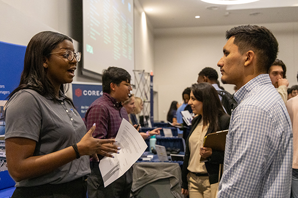 Female employer speaking enthusiastically to a male student at career fair